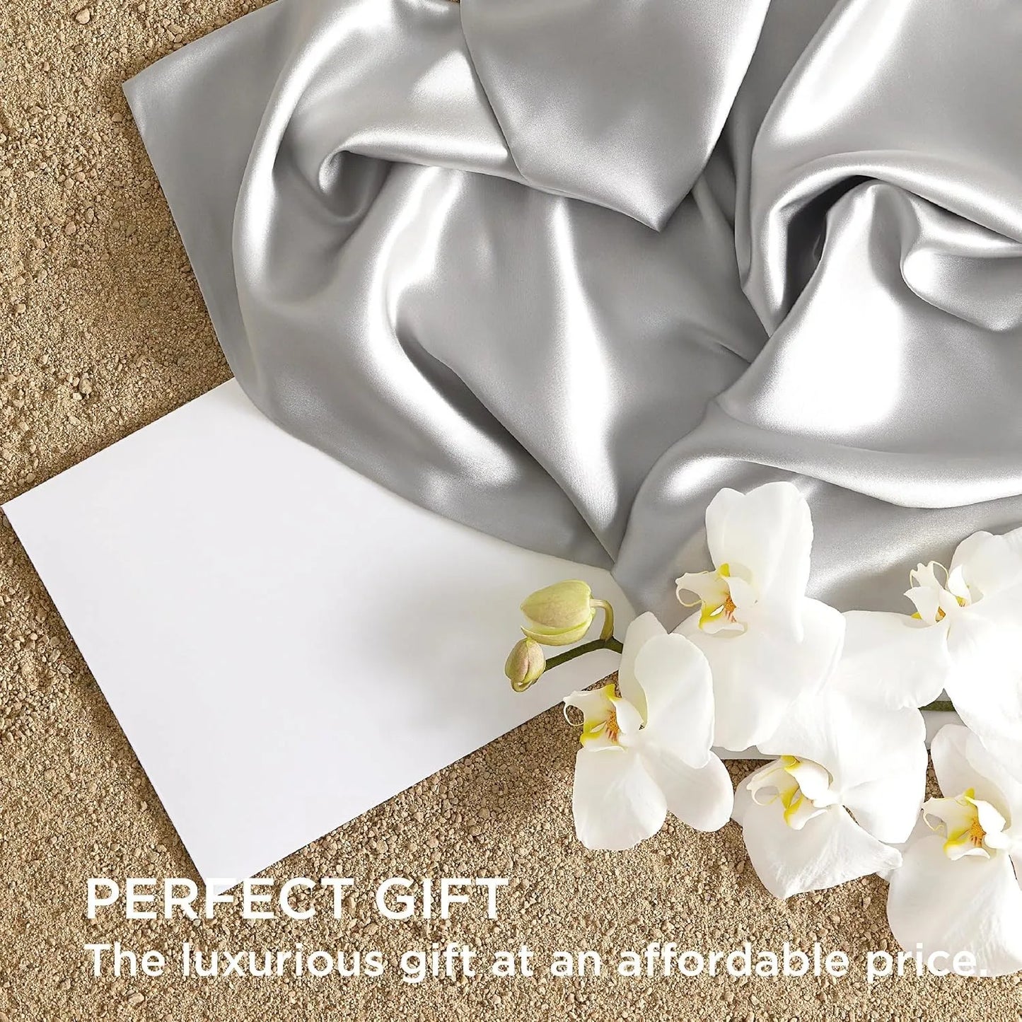 Silver satin fabric with a white card and white flowers on a beige surface, labeled 'Perfect Gift'.