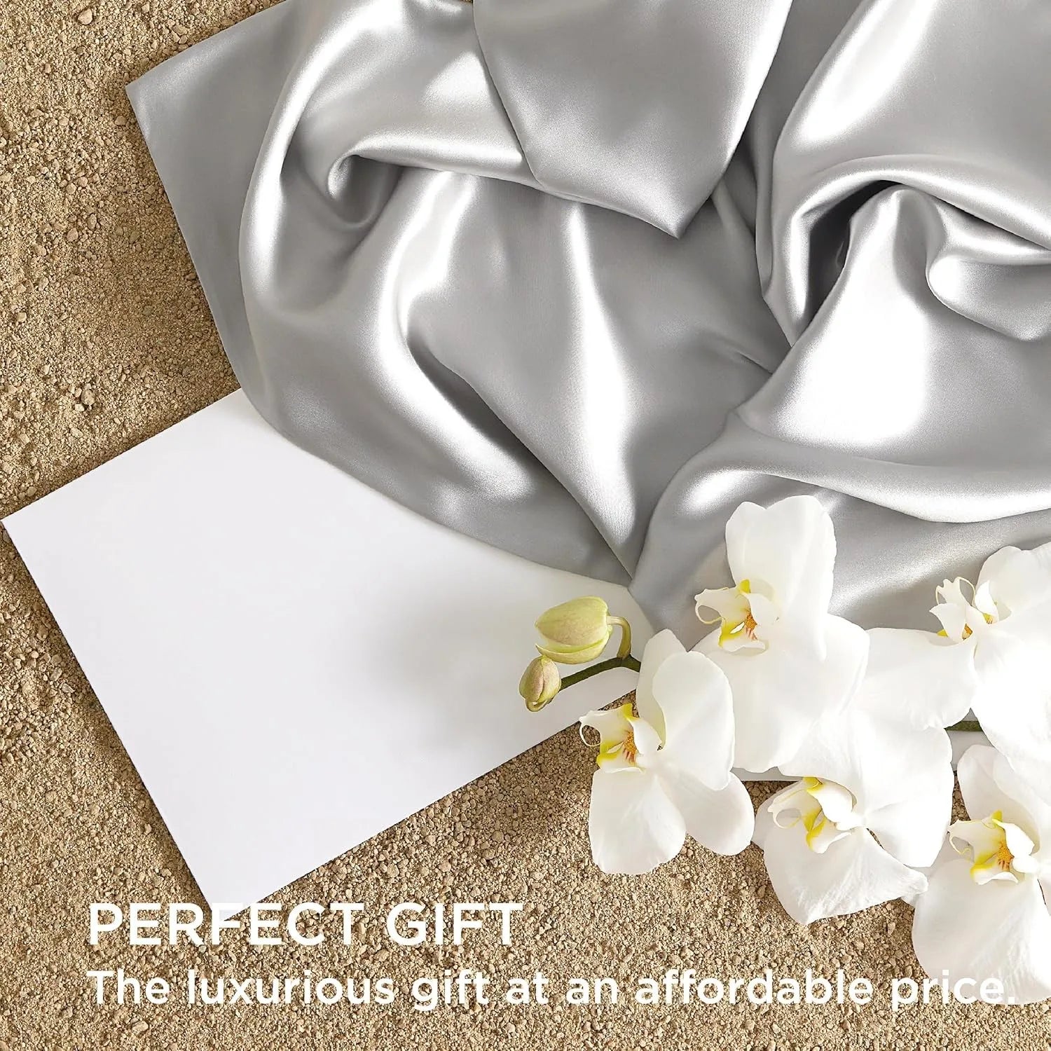 Silver satin fabric with a white card and white flowers on a beige surface, labeled 'Perfect Gift'.