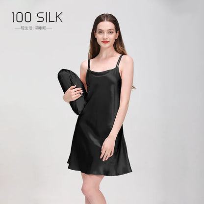 Woman wearing a black silk slip dress holding a matching bag on a gray background with '100 Silk' branding.