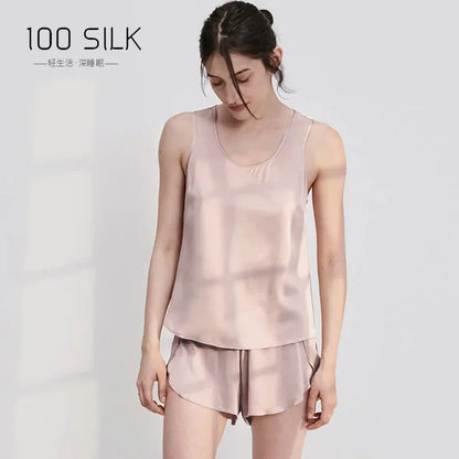 Woman wearing a light pink silk top and shorts set on a white background with '100 SILK' branding.