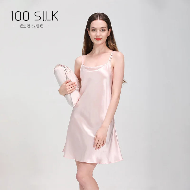 Woman wearing a pink silk slip dress holding a matching bag on a light gray background with '100 SILK' branding.