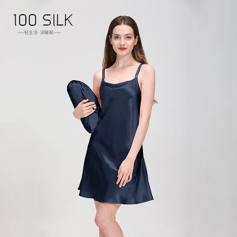 Woman wearing a navy blue silk slip dress holding a matching bag on a light gray background.