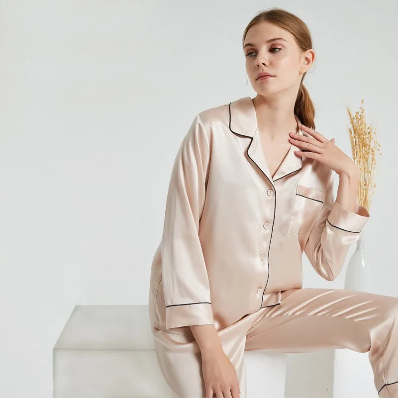 Woman wearing a beige satin pajama set holding a small bouquet of wheat against a white background
