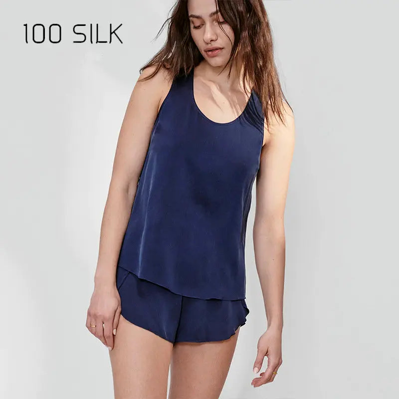 Woman wearing a navy blue silk tank top and shorts on a white background with '100 SILK' text.
