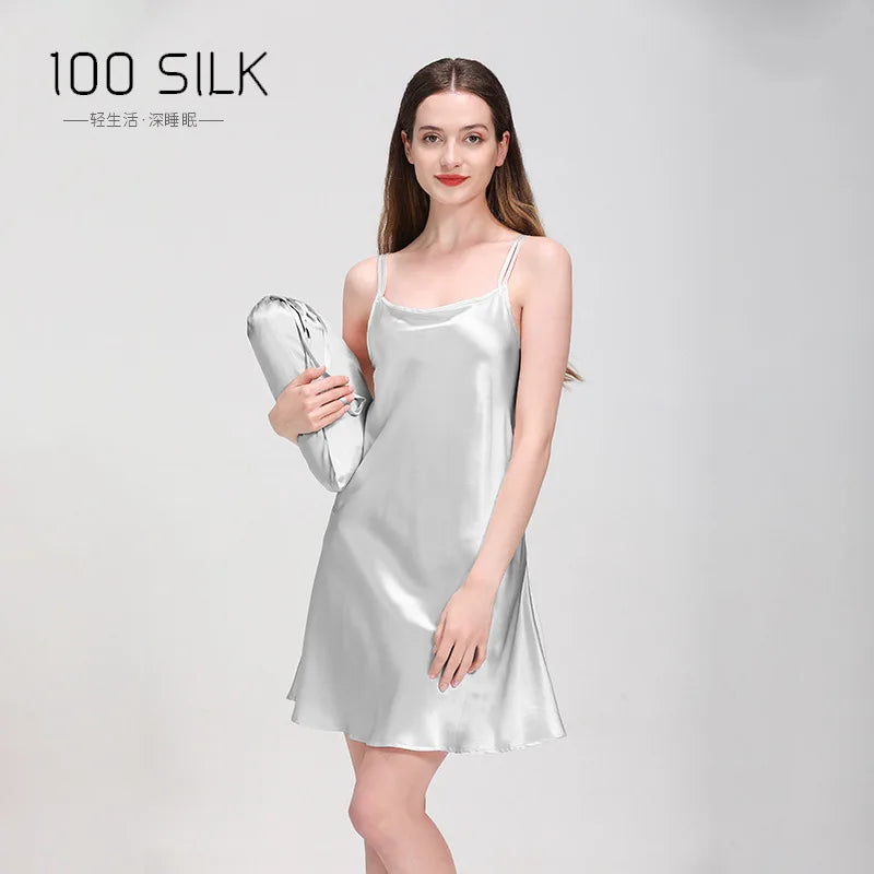 Woman wearing a silver silk slip dress holding a matching bag on a gray background with '100 Silk' branding.