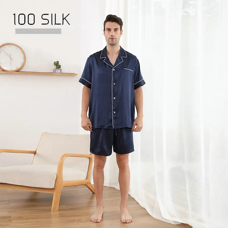Man wearing navy silk pajama set in a room with a white curtain and wooden chair.