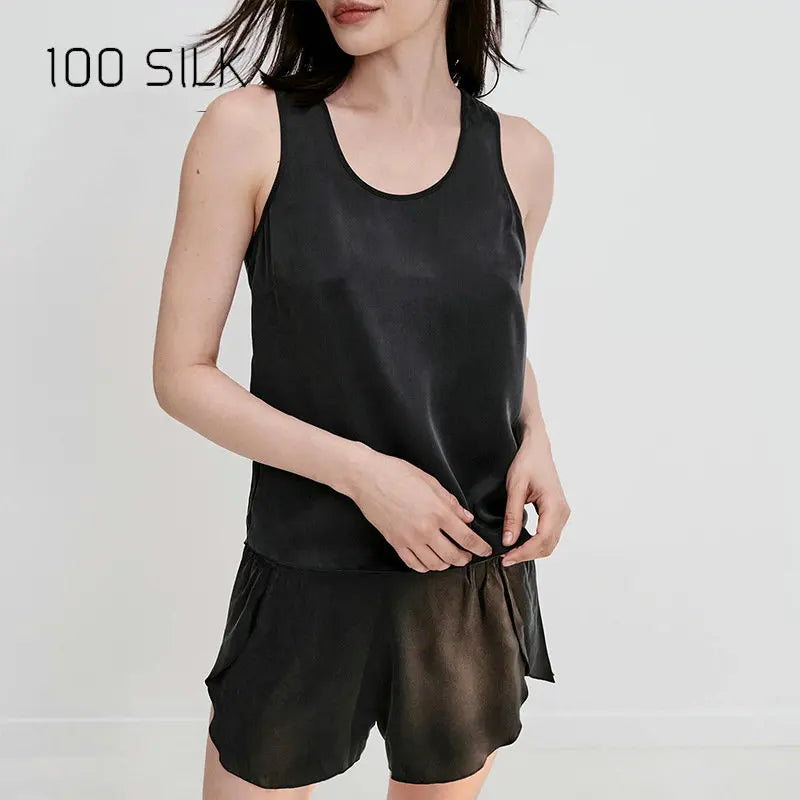 Woman wearing a black satin tank top and shorts with '100 SILK' branding.