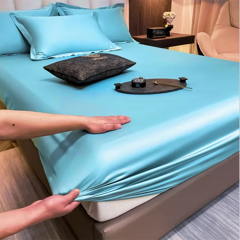 Person stretching a blue satin sheet over a bed with decorative items on top.
