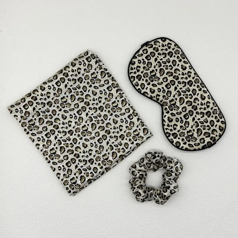 Set of leopard print items including a pouch, eye mask, and scrunchie on a white background
