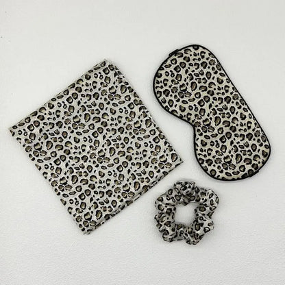 Set of leopard print items including a pouch, eye mask, and scrunchie on a white background