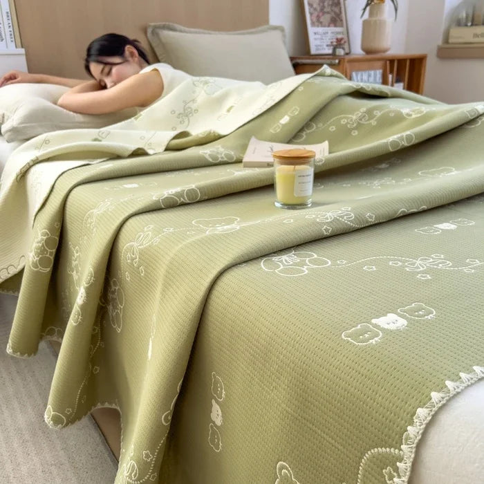 Person lying on a bed with a green patterned blanket, candle, and books.