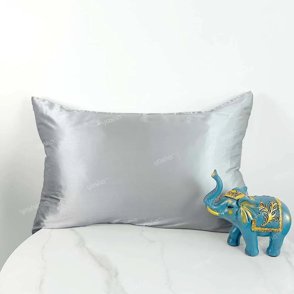 Decorative blue elephant figurine next to a gray satin pillow on a white surface.